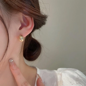 Close-up of a model wearing minimalist golden bean-shaped polished metal stud earrings