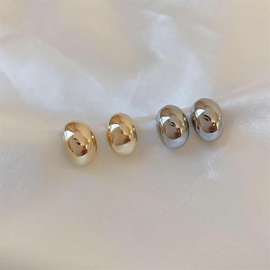 Polished gold and silver bean-shaped stud earrings on white silk fabric background