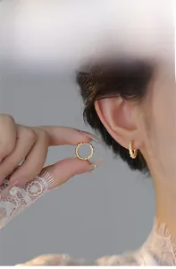 Detail showing high-quality golden twisted hoop earrings on a model and hand for scale