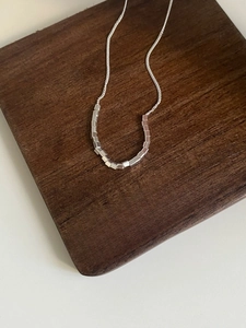 Close-up of minimalist S925 sterling silver necklace with small cube pendant on wood