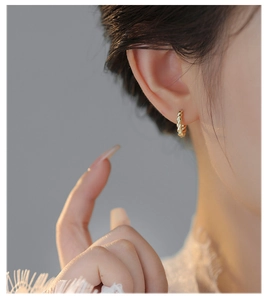 Close-up of elegant gold twisted hoop earrings worn by a model for a stylish aesthetic