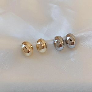 Polished gold and silver oval stud earrings displayed on elegant white silk fabric
