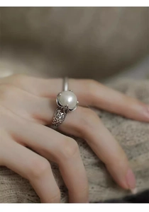 Detail of vintage S925 silver pearl ring with hollow floral patterns worn on finger