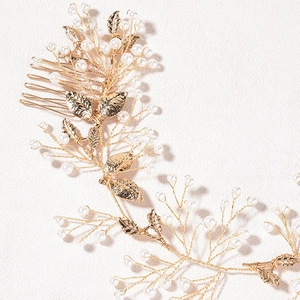 Macro detail of bridal hair comb featuring golden metal leaves and white pearls