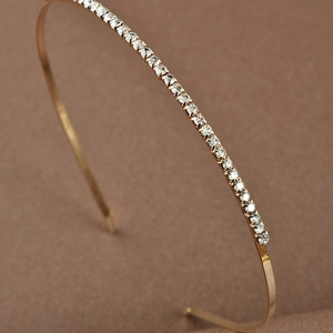 Macro shot of gold-plated alloy headband with clear rhinestones on dark textured background