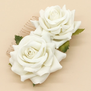 Close-up of white velvet rose hair comb with green leaves on a golden metal base