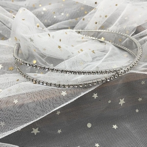 Détail d'un serre-tête double en strass argenté posé sur un tulle blanc avec paillettes dorées