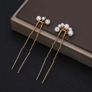 Detailed view of handmade gold bridal hair pins with elegant white pearls on a dark box