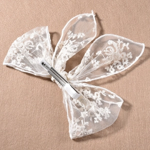 Elegante pasador de pelo con lazo de encaje beige bordado sobre fondo texturizado