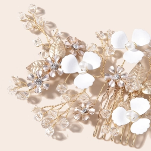 Macro detail of bridal hair comb with gold leaves, white enamel flowers and pearls