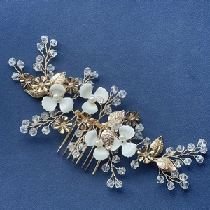 Handmade bridal hair comb with gold leaves, white flowers, and pearls on blue background