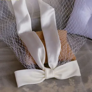 Detail shot of white satin bow veil with mesh on a rustic linen and soft white cushion