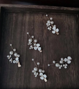 Detailed close-up of five white floral hair clips with pearls and gold wire on wood