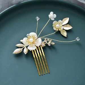 Détail d'un peigne à cheveux de mariée doré avec fleurs blanches, perles et strass sur plateau