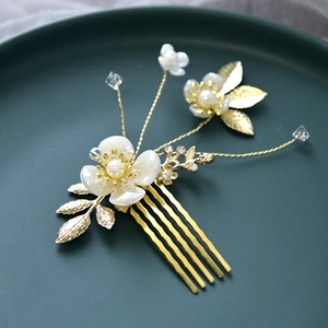 Détail d'un peigne de mariée avec fleurs en résine blanche, perles et feuilles dorées