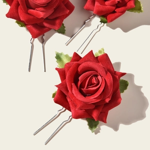 Detailed view of three red rose hair pins with velvet petals and green leaf accents