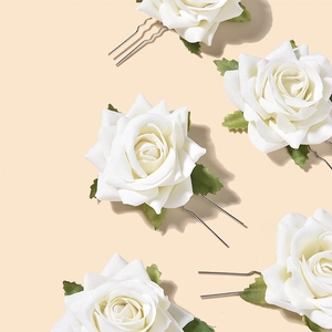Close-up of white rose hair pins with fabric petals and green leaves for bridal styling