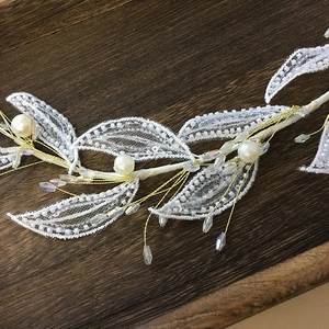 Elegant bridal headpiece with white lace leaves, sequins, and pearls on a wooden surface