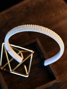 Close-up of elegant bridal pearl headband on a gold stand with a dark wood background