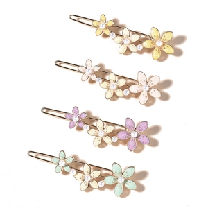 Detail of four colorful enamel flower hair clips with pearls and gold metal base