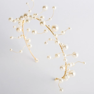 Handmade bridal headpiece with white pearls and gold wire branches on a gray background