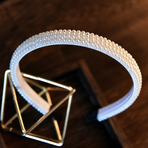 Elegant white pearl headband for brides on a gold display stand with dark wood background