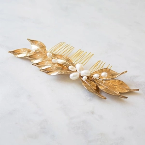 Close-up of golden alloy leaf hair comb with handcrafted pearls on marble surface
