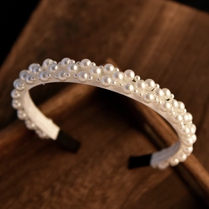 Macro detail of the white pearl bridal headband showing dense layered pearls on a dark wood