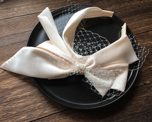 Detail of bridal headband with cream satin bow, delicate mesh veil, and pearl embellishments