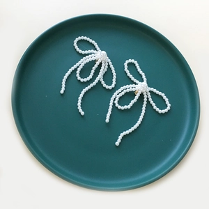 Eleganti orecchini a clip con fiocco in perle fatti a mano su un piatto di ceramica verde