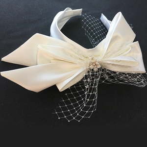 Detail of white satin headband with oversized bow, mesh veil, pearls and rhinestones