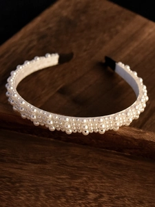 Detail of elegant white pearls on a silk wrapped headband placed on a wooden tray