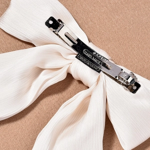 Detail of white pleated chiffon bow hair clip showing silver metal spring fastener
