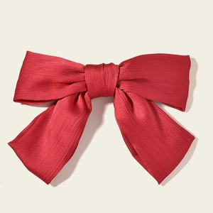 Detail of red bridal bow hair clip showing vertical pleated chiffon fabric texture