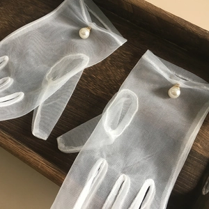 Detail of white mesh wedding gloves with elegant pearl accent on vintage wood tray