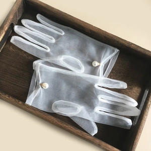 Elegant white mesh wedding gloves with pearl decor on a vintage wooden tray