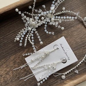 Silver bridal headband and long tassel earrings set with crystal beads on a wooden tray