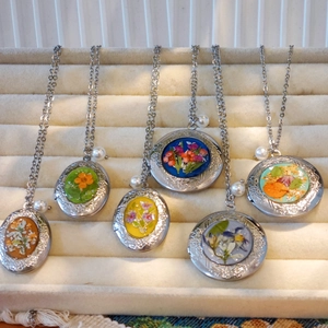 Detail van handgemaakte medaillonkettingen met gedroogde bloemen en parelaccenten