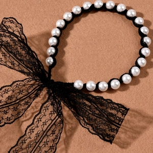 Detail of vintage pearl headband featuring elegant black lace bow on textured background