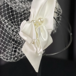 White satin bridal headband with pearls and vintage mesh veil on a black background