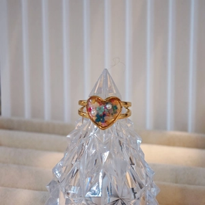 Dettaglio dell'anello a cuore dorato fatto a mano con veri fiori secchi e perle in resina