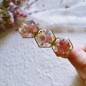 Handmade resin hair clip featuring pink dried flowers, pearls, and gold foil in hexagon frames