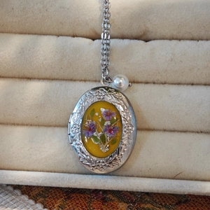 Detail van ovale roestvrijstalen medaillon met gele hars en paarse droogbloemen
