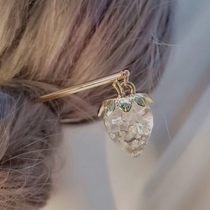 Nahaufnahme eines goldenen Haarstabs mit einem zarten transparenten Erdbeeranhänger