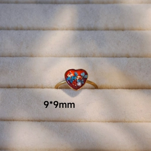 Detail eines herzförmigen Rings mit blauen Trockenblumen und Blattgold in rotem Harz