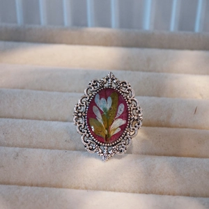 Close-up of handmade vintage ring with red oval dried flower resin and silver frame