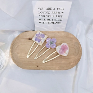Detail view of handmade resin hair clips with dried flowers and pearls on wooden tray