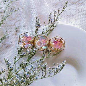 Detail of resin hair clip with pink dried flowers, gold foil, and pearls in hex frames