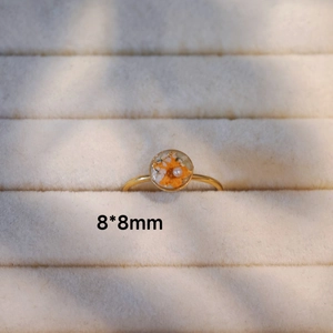 Detaillierte Makroansicht eines 8x8mm Goldrings mit orangefarbener Trockenblume und Perle