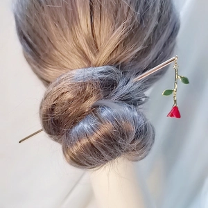 Detailed view of a metal hair pin with a red rose pendant in a brown hair bun